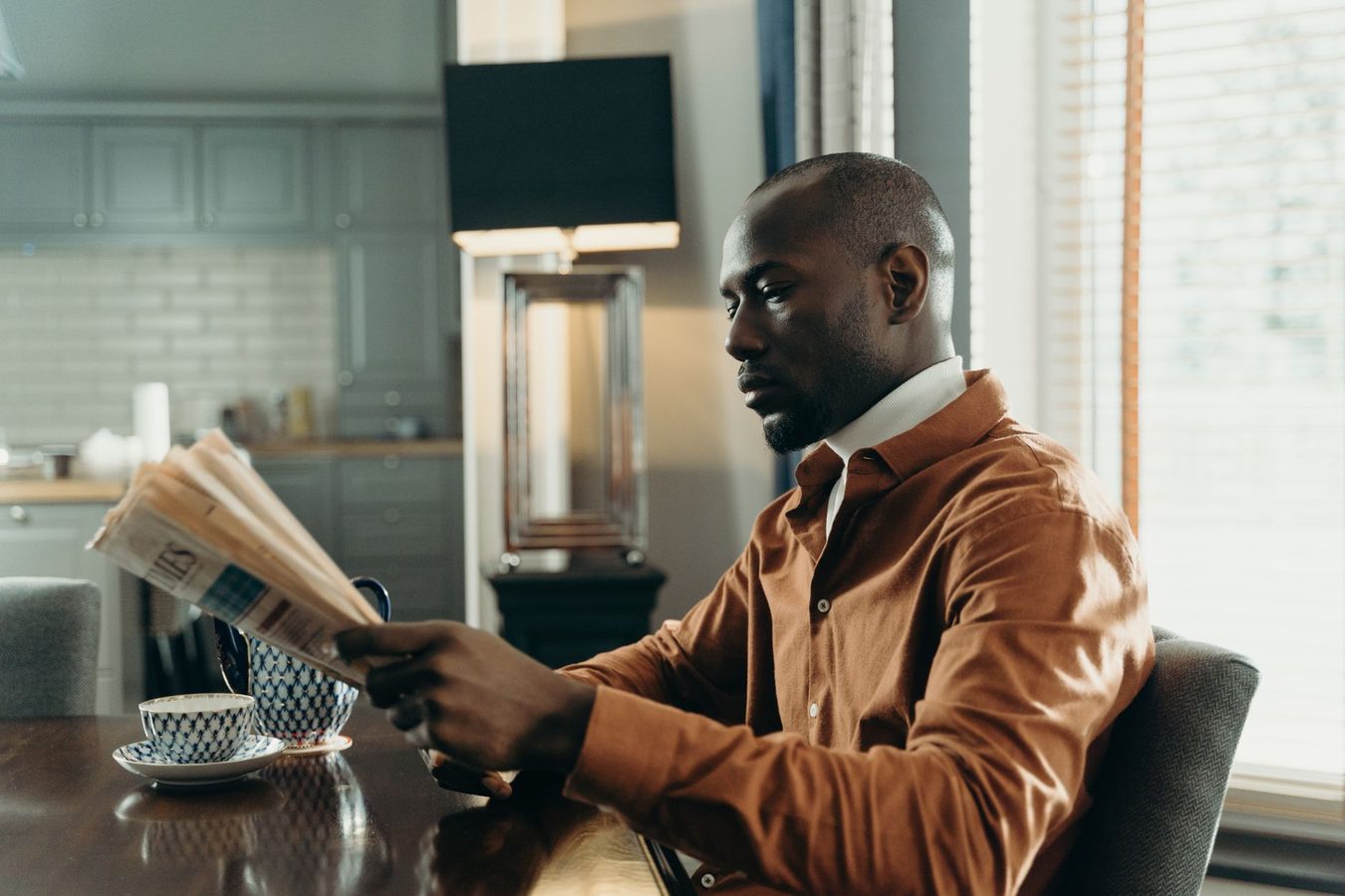A reader with a folded newspaper and coffee at a kitchen table